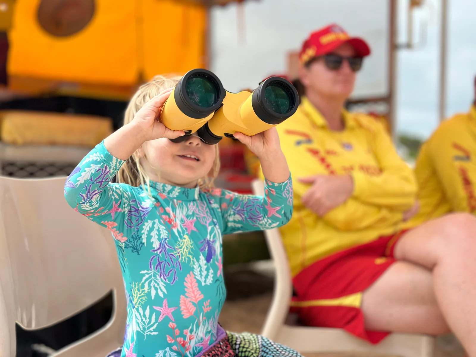 Child using patrol binoculars with Fingal Beach lifesavers in patrol uniform behind